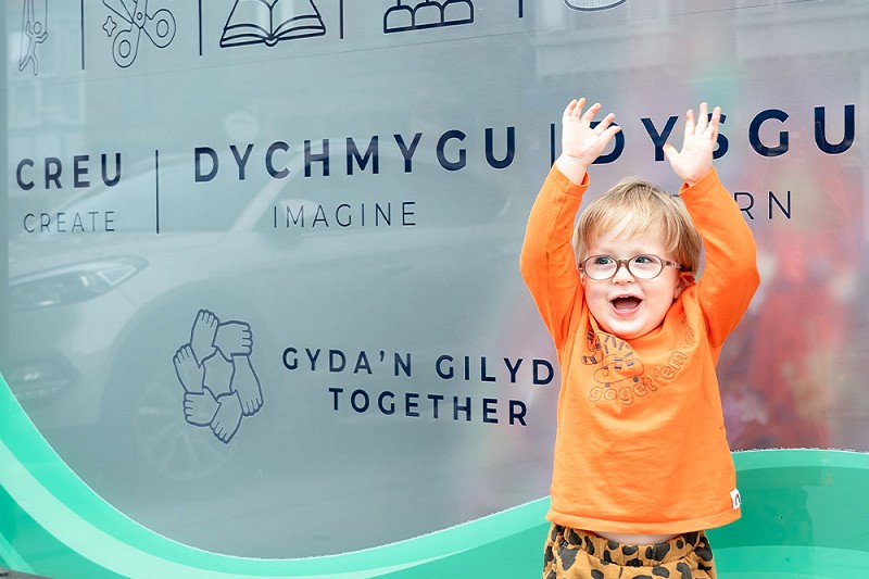 Happy excited young boy outside Creadigol Colwyn Creative sign which reads Create, Imagine, Learn